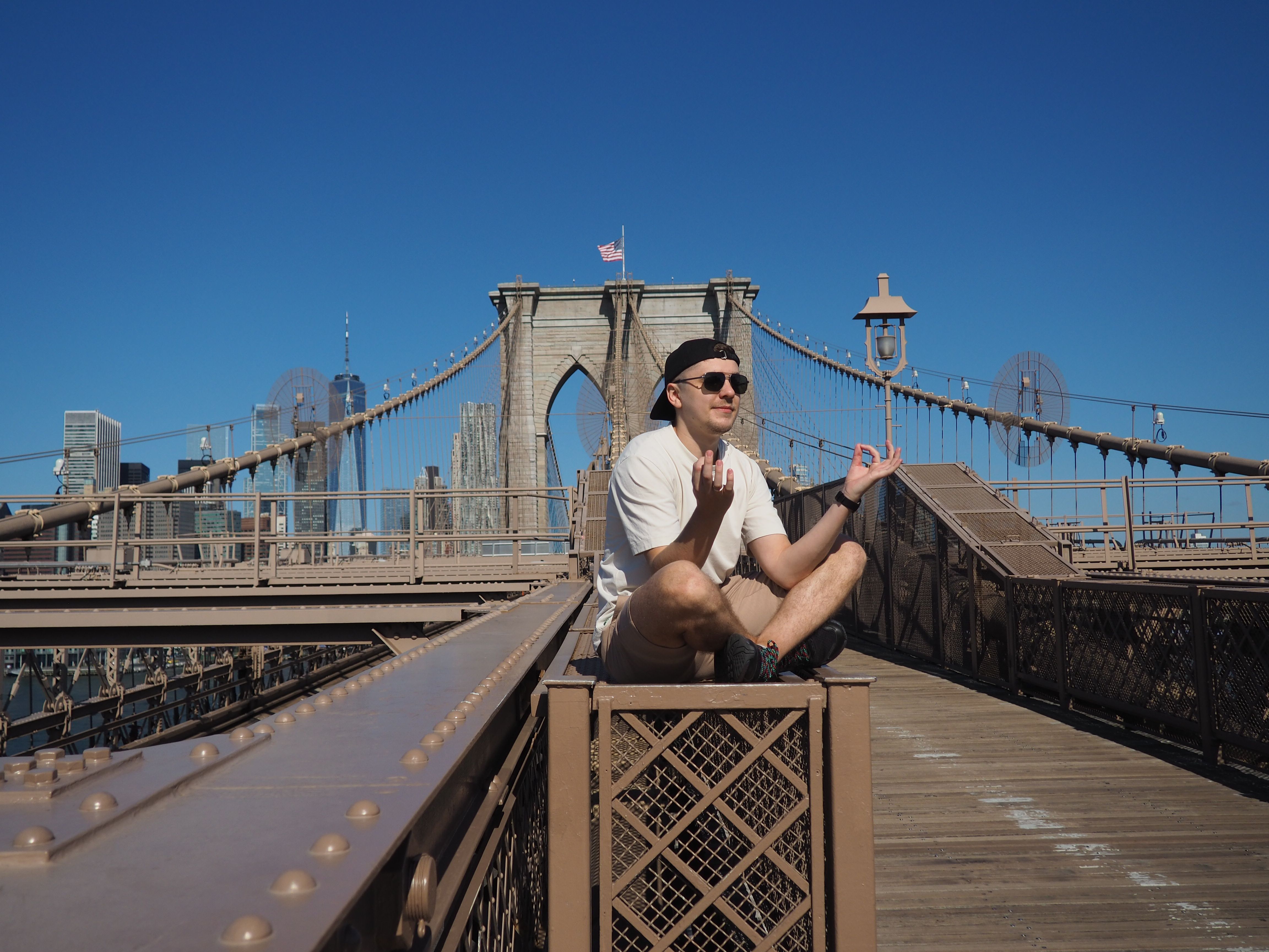 Photo with a man in sunglasses sitting on the bridge, sky in the background.